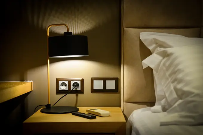 A bedside lamp and crisp white bedding in warm light