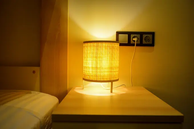 A rattan bedside lamp glowing on an oak table