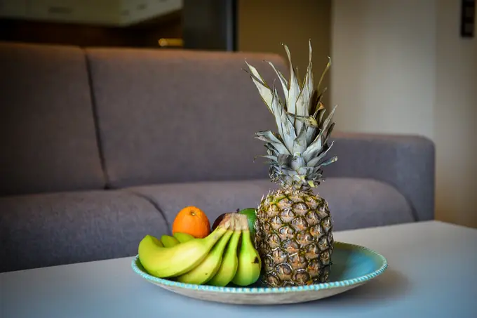 A bowl of pineapple, bananas and oranges on the coffee table