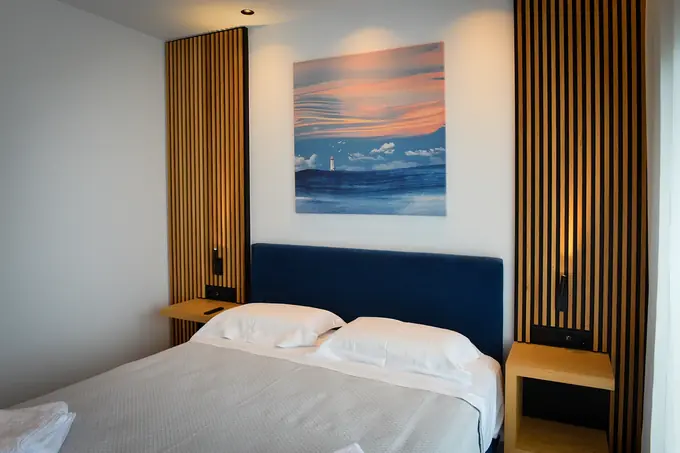 Double bed with a blue headboard under a sunset painting
