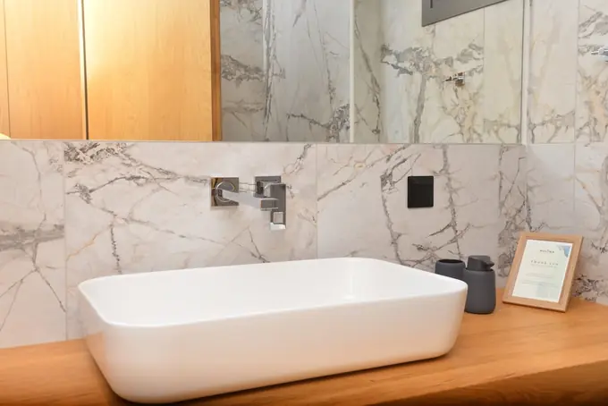 White basin on an oak counter against marble walls